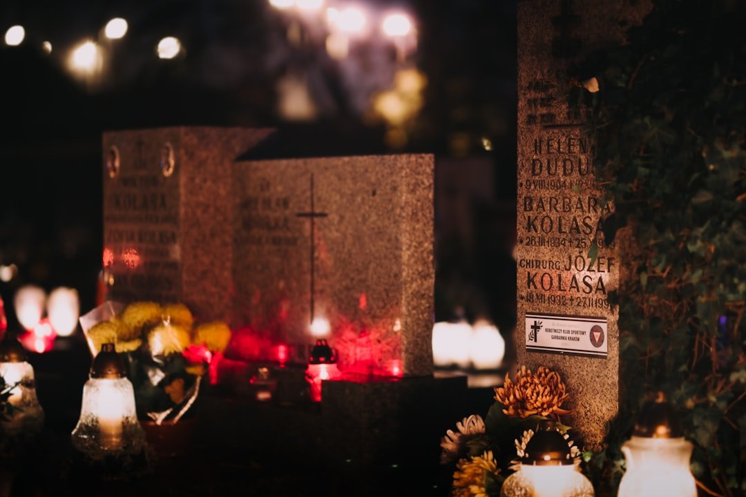 Candlelit grave markers with flowers at night, remembering loved ones.