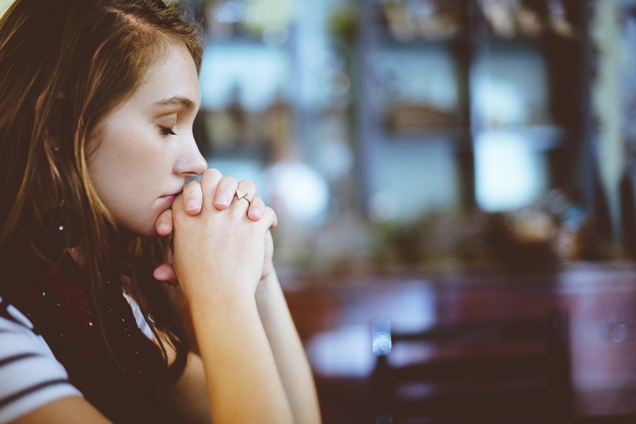 Woman praying, hands clasped, mourning a loss, finding hope.