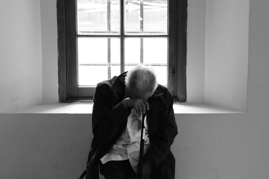 Elderly man, window: grief after decades of companionship.